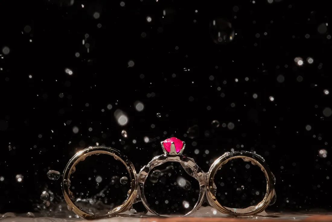 Three wedding rings catching the light amid scattered water droplets